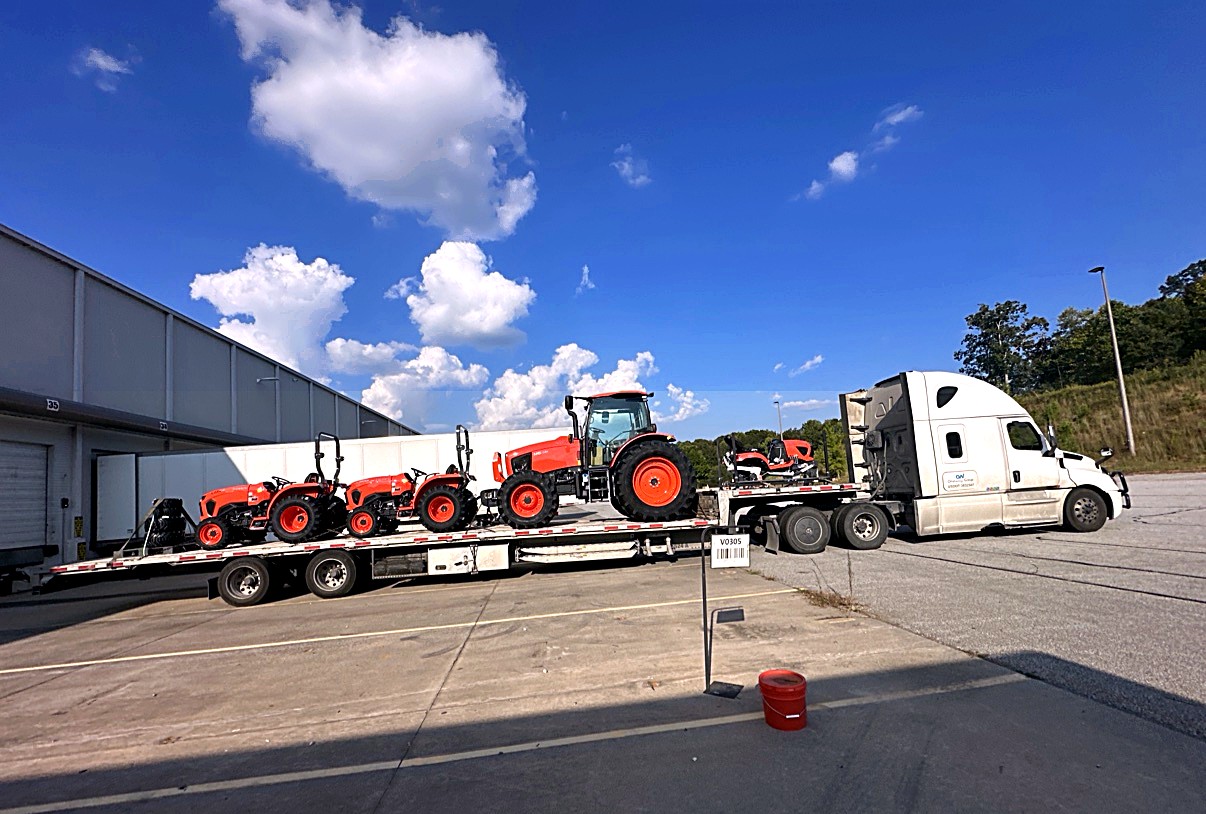 Oneway Group stepdeck loaded with orange Kubota tractors at a warehouse dock