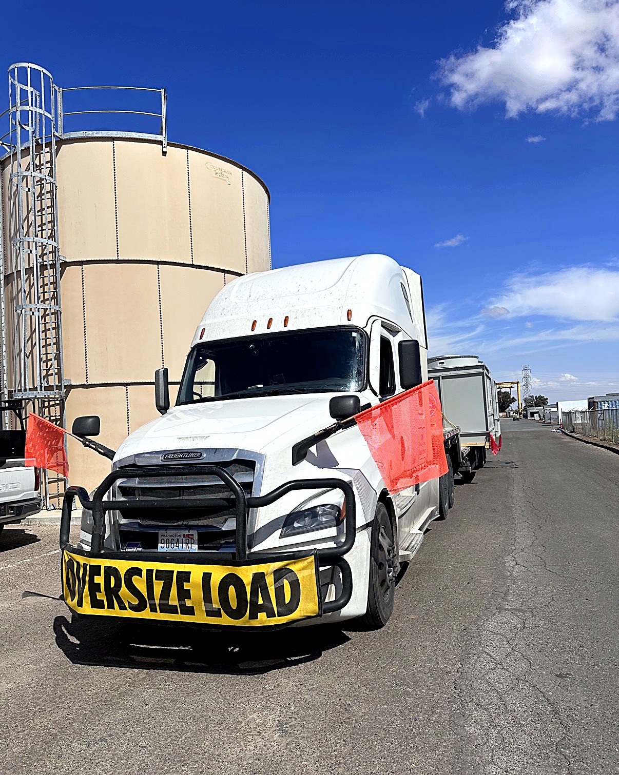 Oneway Group Freightliner with yellow OVERSIZE LOAD banner and orange flags at an industrial tank site